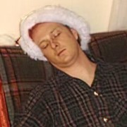 Man with closed eyes wearing a Santa hat and plaid pajamas
